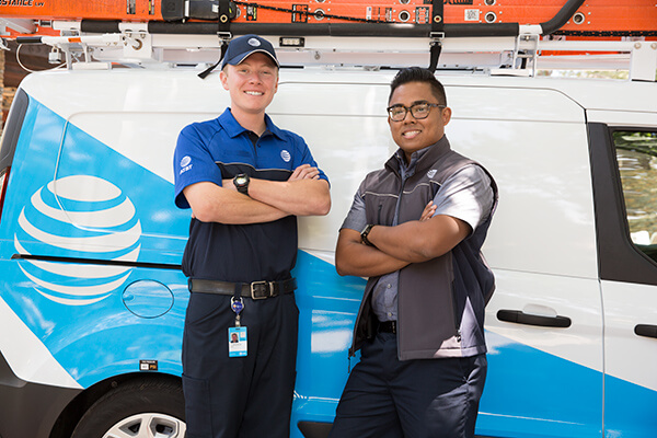 Two men, both employees of AT&T standing together witht their arms crossed while leaning against an AT&T service van. 